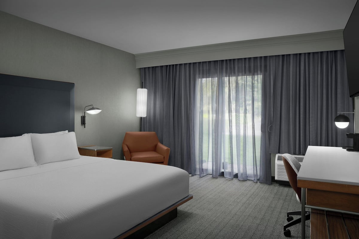 Una habitación de hotel con una cama grande, un escritorio, una silla naranja y un ventanal con cortinas.