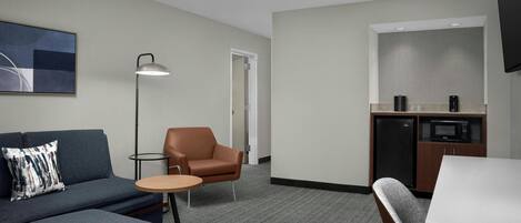 Habitación de hotel con sofá, sillón, mesita redonda y zona de kitchenette.