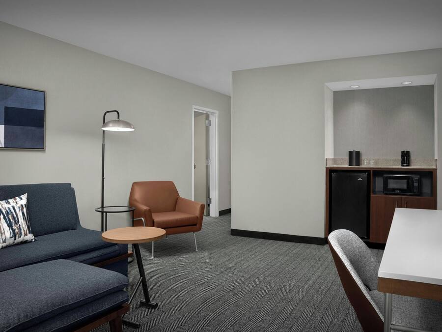 Habitación de hotel con sofá, sillón, mesita redonda y zona de kitchenette.