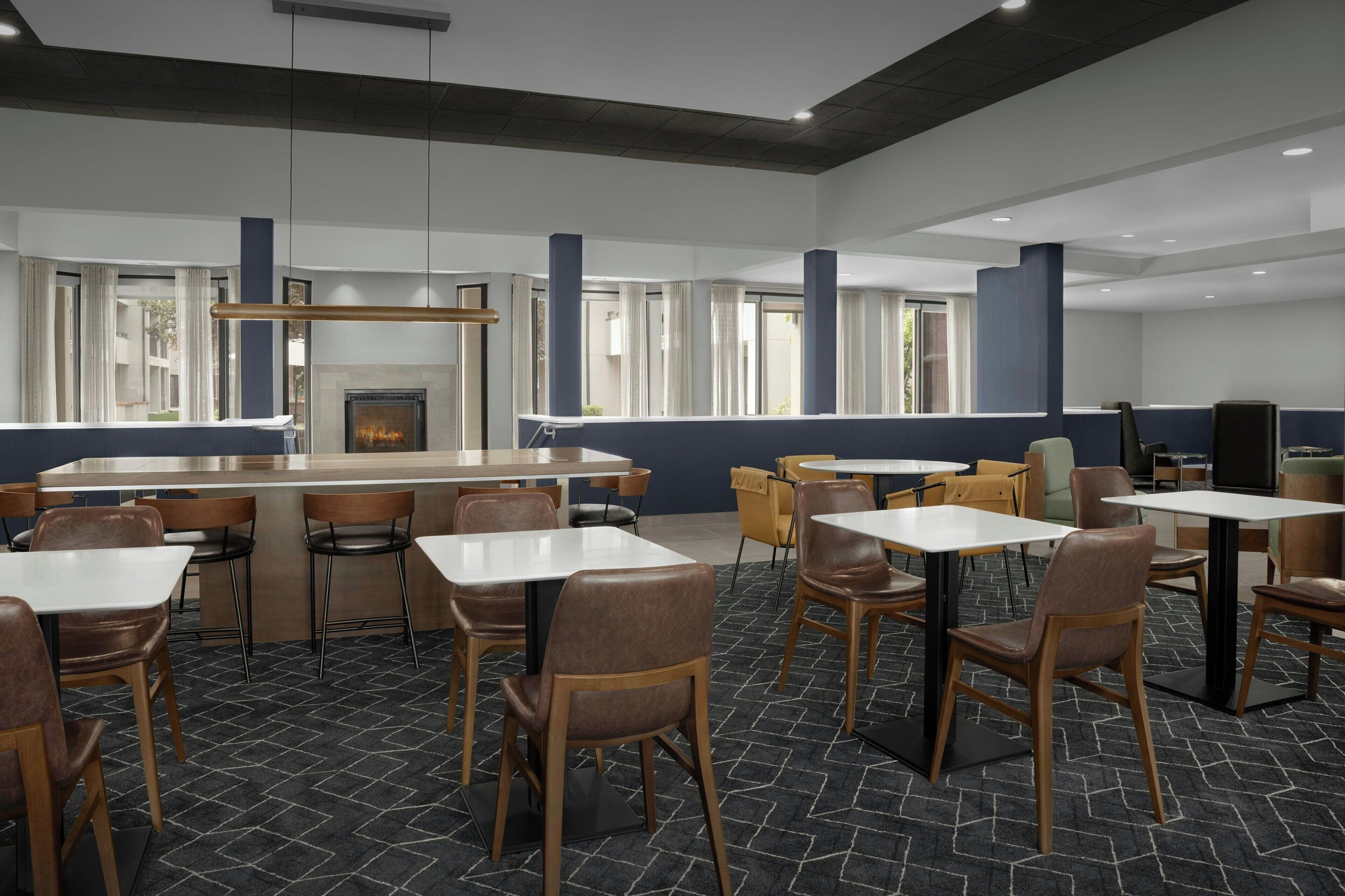 A modern dining area with a bar, multiple tables and chairs, and a fireplace.
