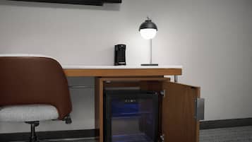 A compact office setup with a desk, a coffee machine, a lamp, and a built-in mini-fridge.