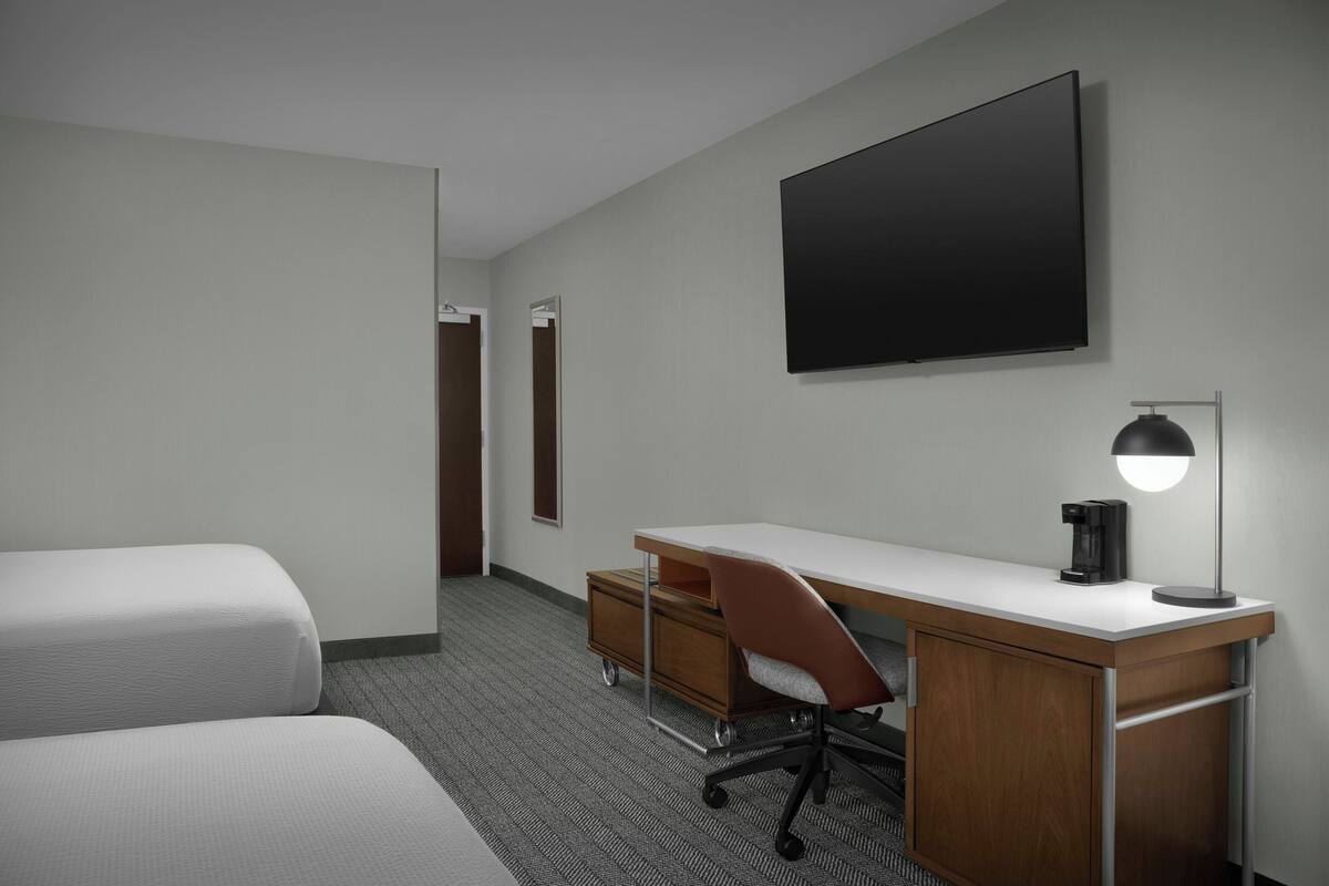 Habitación de hotel con cama, escritorio con silla, televisor de pantalla plana y cafetera.