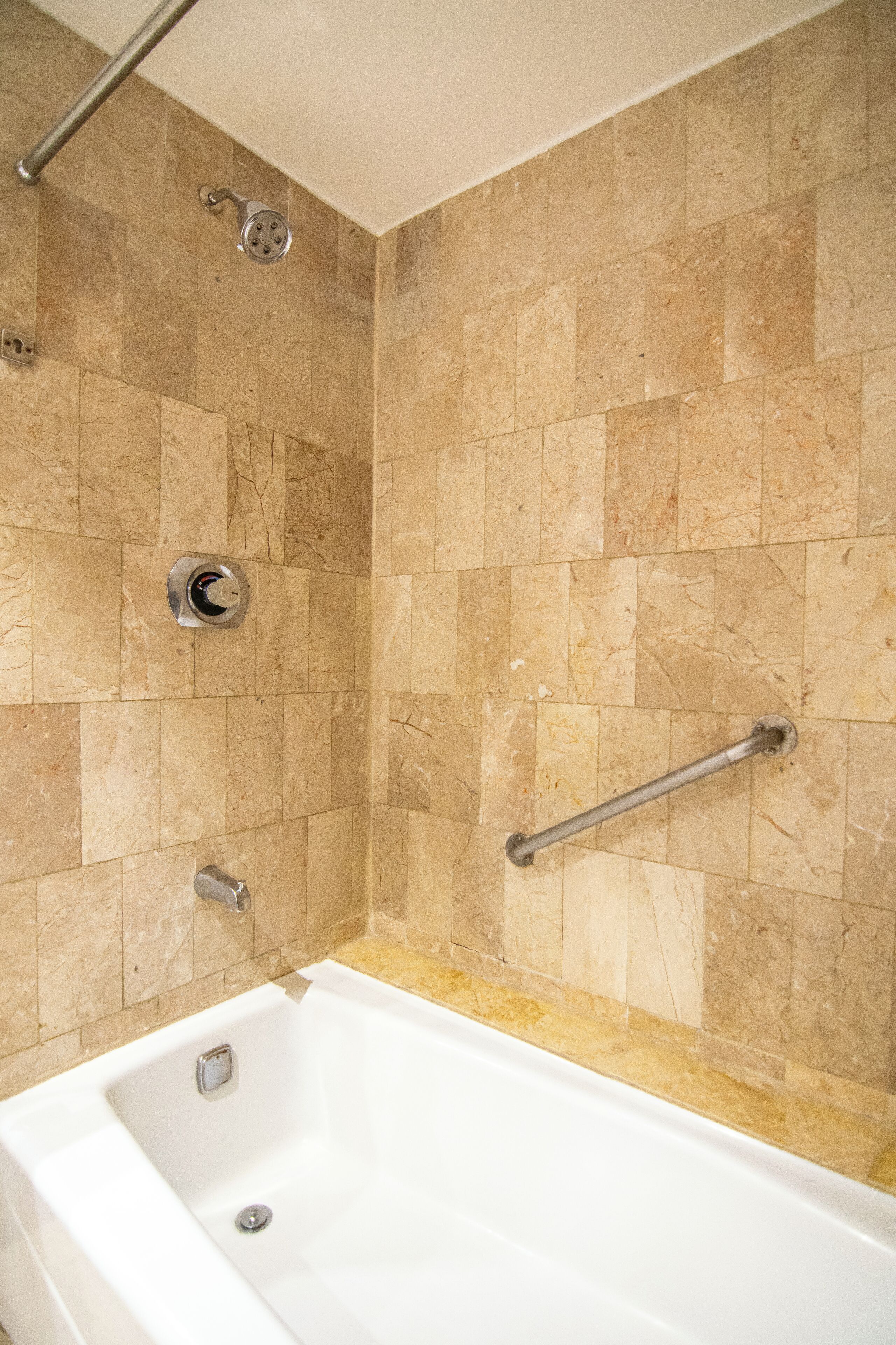 A bathroom with a bathtub, a showerhead, and a grab bar.