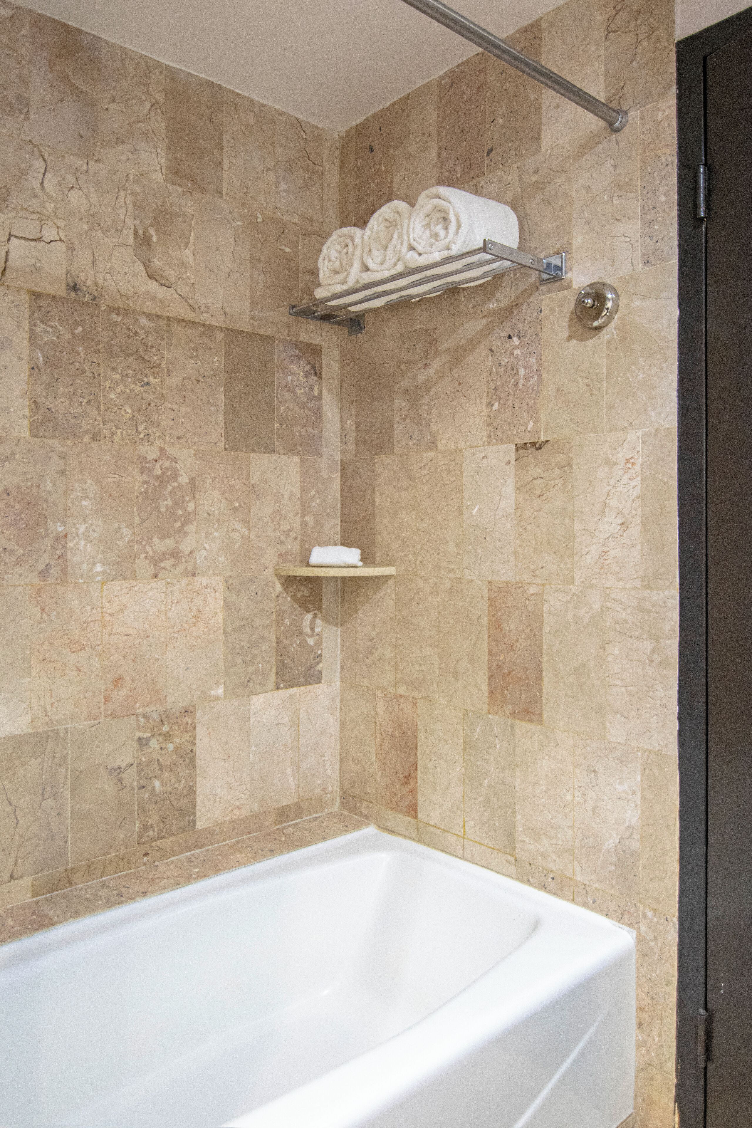 A bathroom with a bathtub, marble walls, and a towel rack with towels.