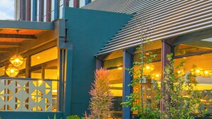 Um edifício moderno com fachada azul, grandes janelas e área externa coberta com vasos de plantas.
