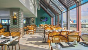 Un amplio comedor interior con techos altos y grandes ventanales que ofrecen vistas a la ciudad.