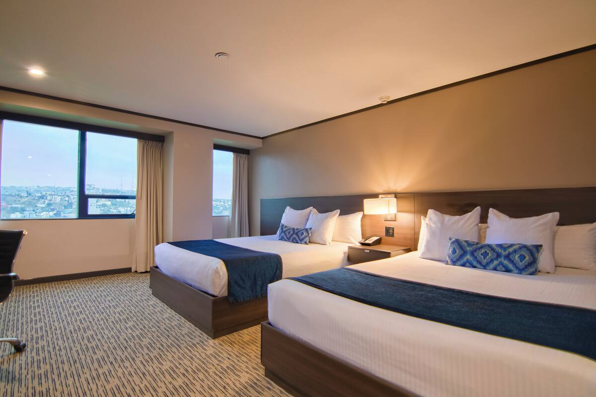 Ein Hotelzimmer mit zwei Betten, Blick auf die Stadt und einem Schreibtisch mit Stuhl.