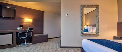 Une chambre d’hôtel comprenant un lit, un bureau avec une chaise, une télévision et un grand miroir.