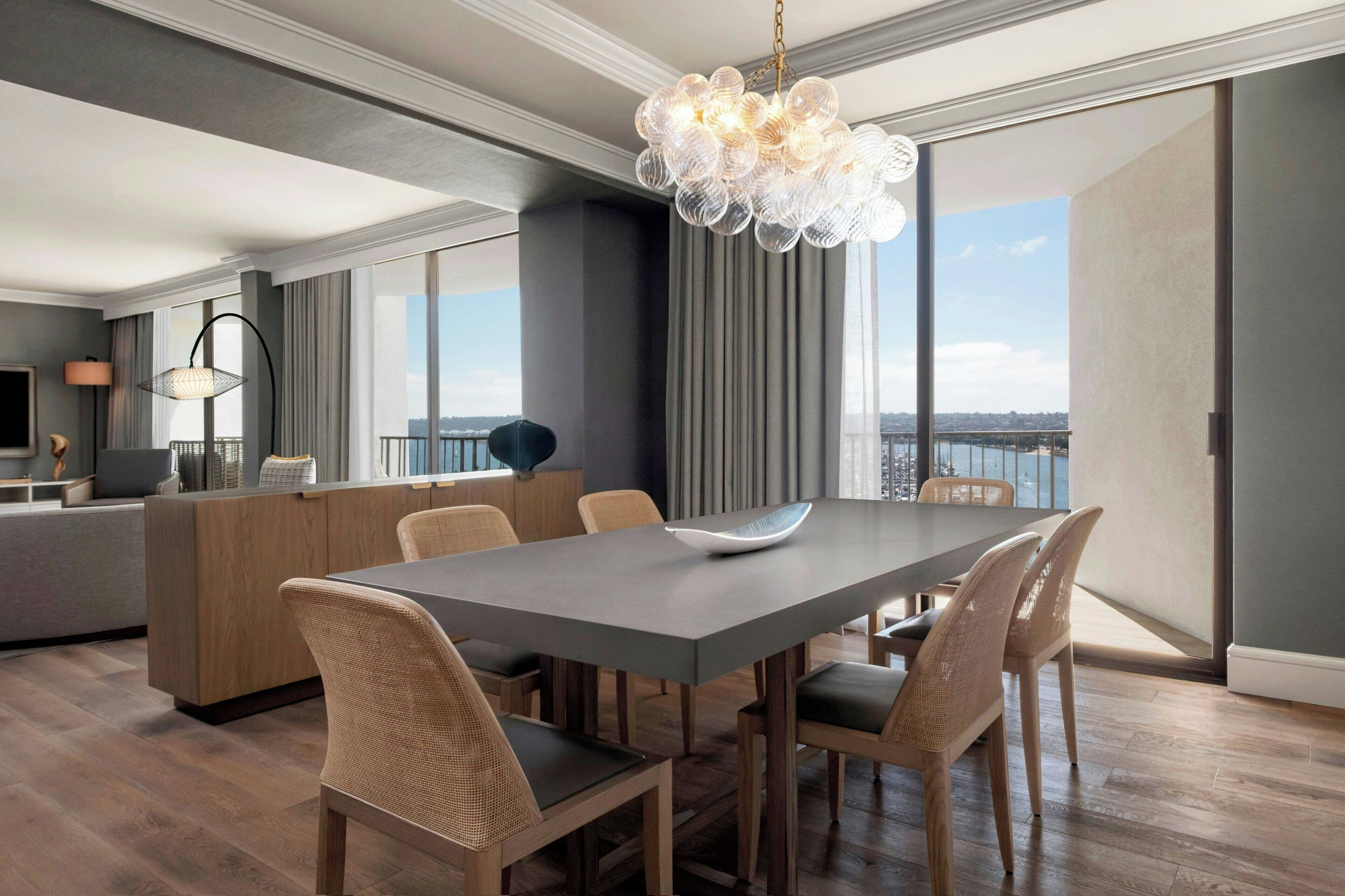 A modern dining area with a large table, wicker chairs, a central island, and a decorative chandelier.