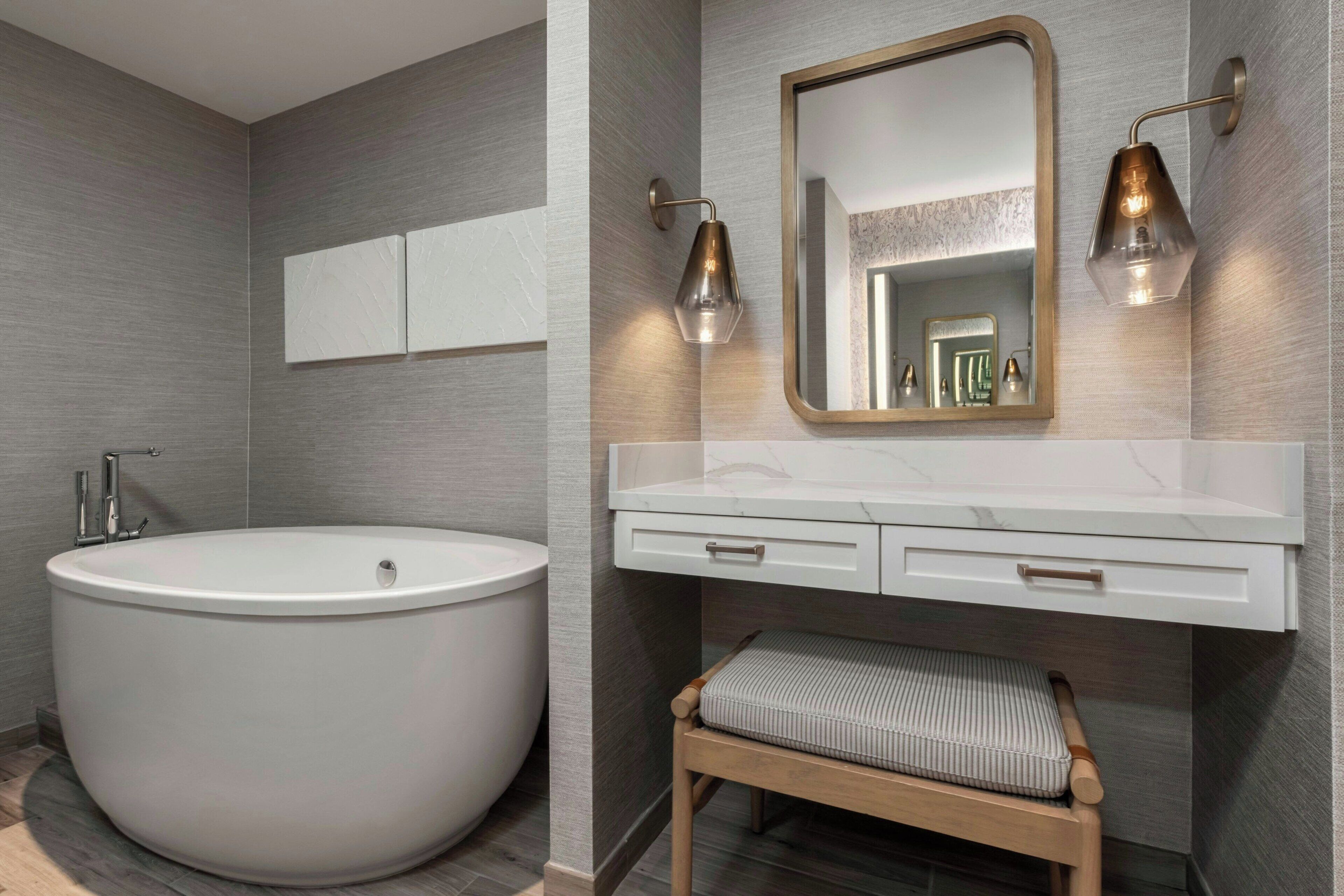 A modern bathroom with a freestanding bathtub, a vanity with a mirror, and two wall-mounted sconces.