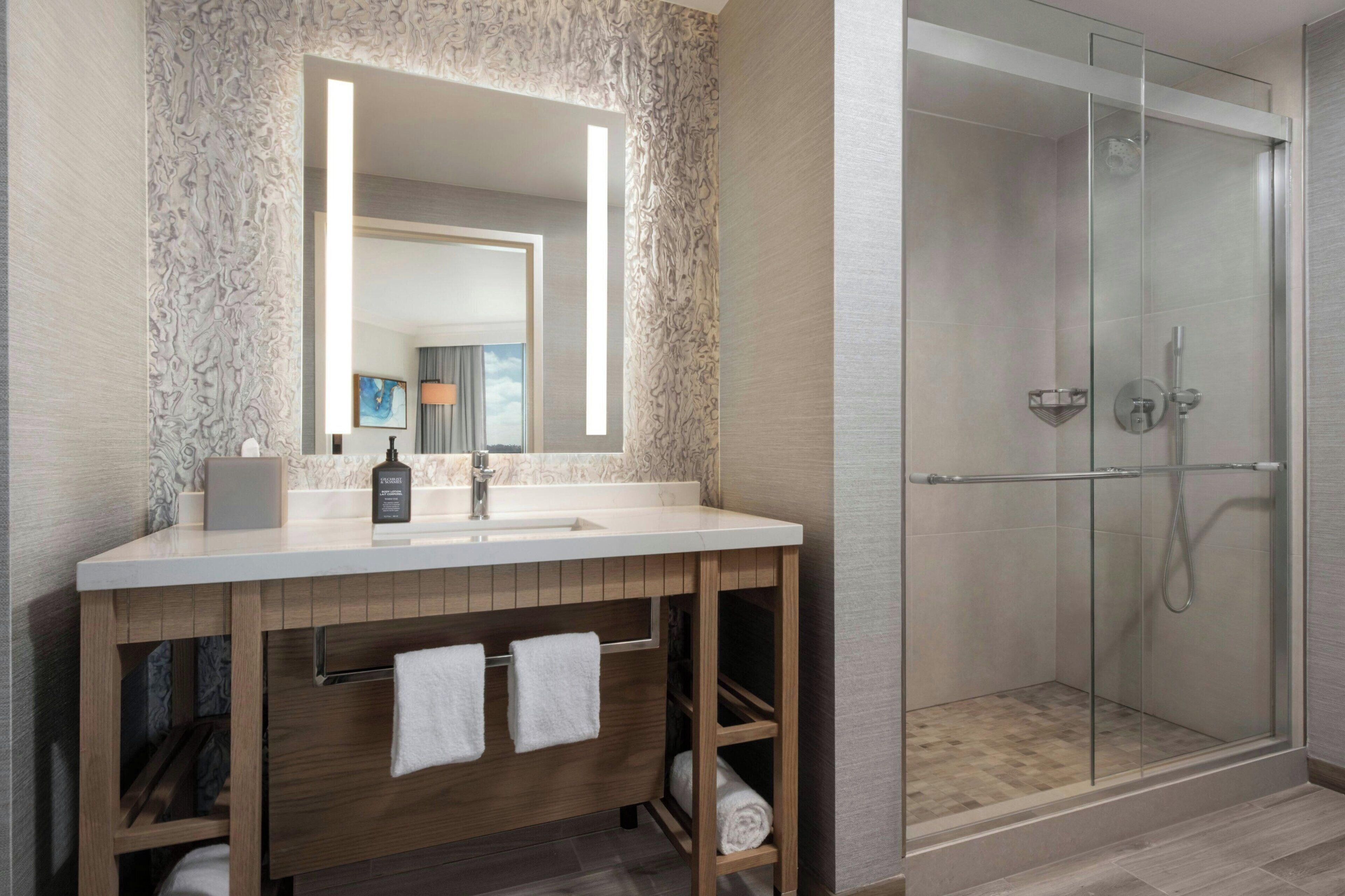 A modern bathroom with a marble backsplash, a large mirror, a wooden vanity, and a glass-enclosed shower.