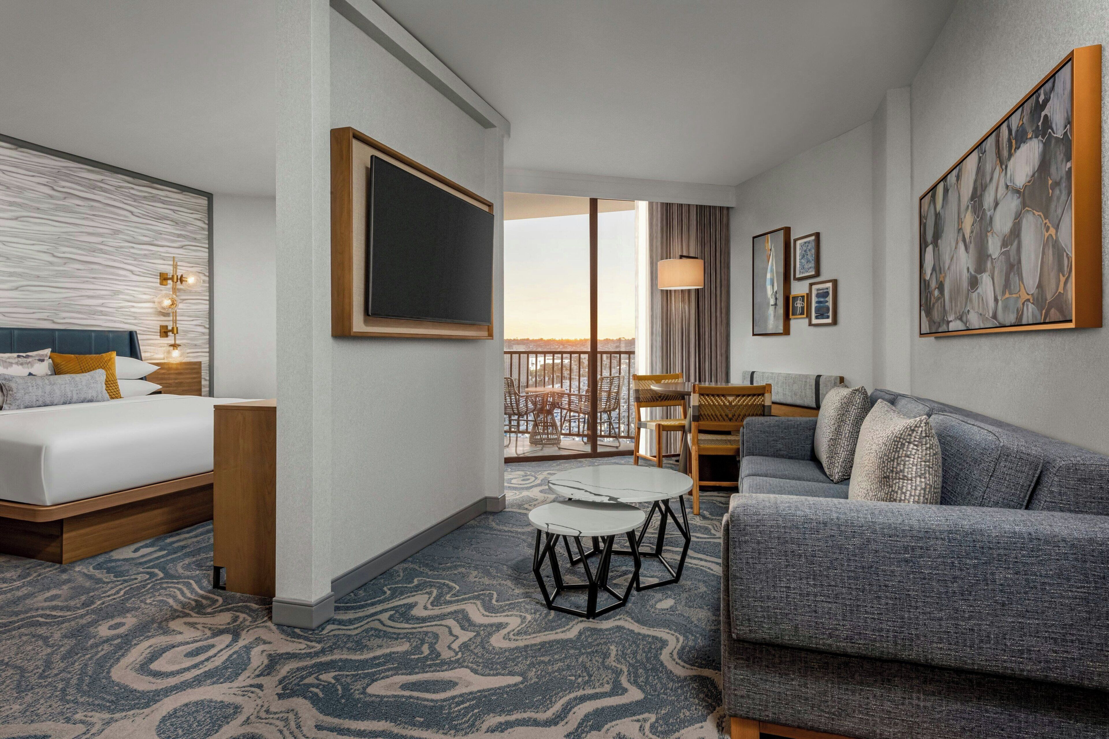 A hotel room with a bed, a sofa, a dining table, and a balcony with a view.