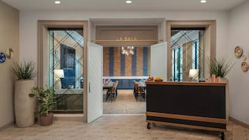 Una hall d'albergo moderna con zona ristorazione, una reception e un'ampia pianta in vaso.
