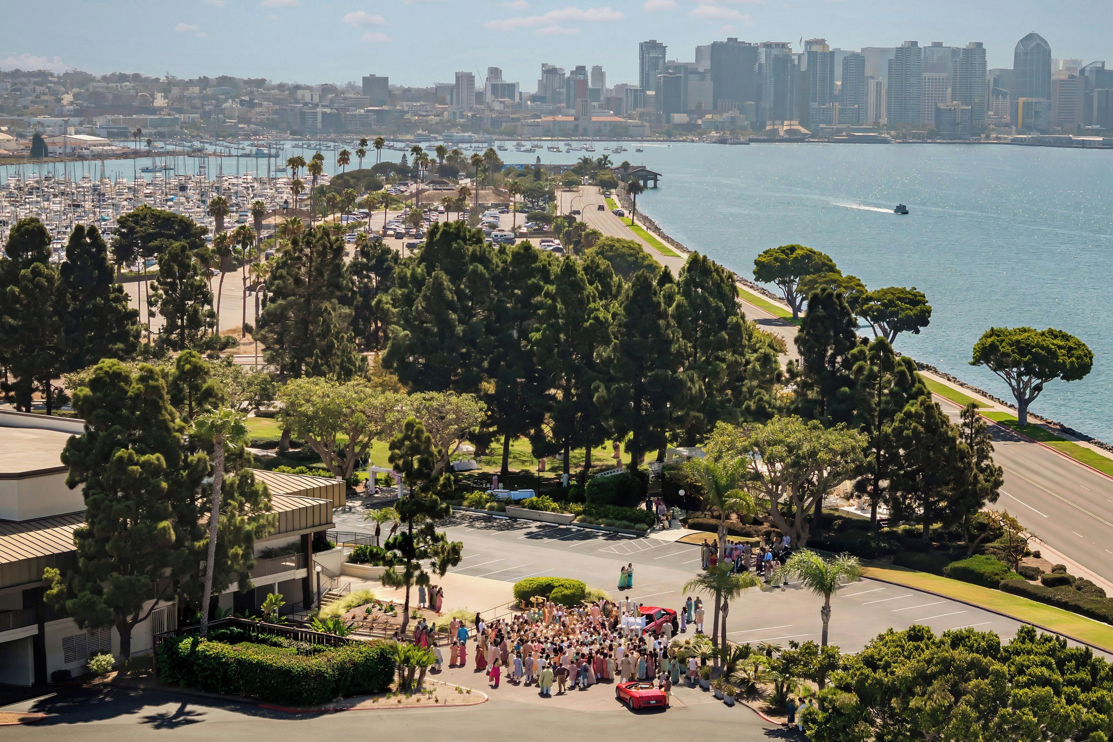 A coastal cityscape with a marina, a crowd of people, and a prominent red sports car.