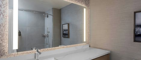 A modern bathroom with a large mirror, a white sink, a shower, and a toilet.