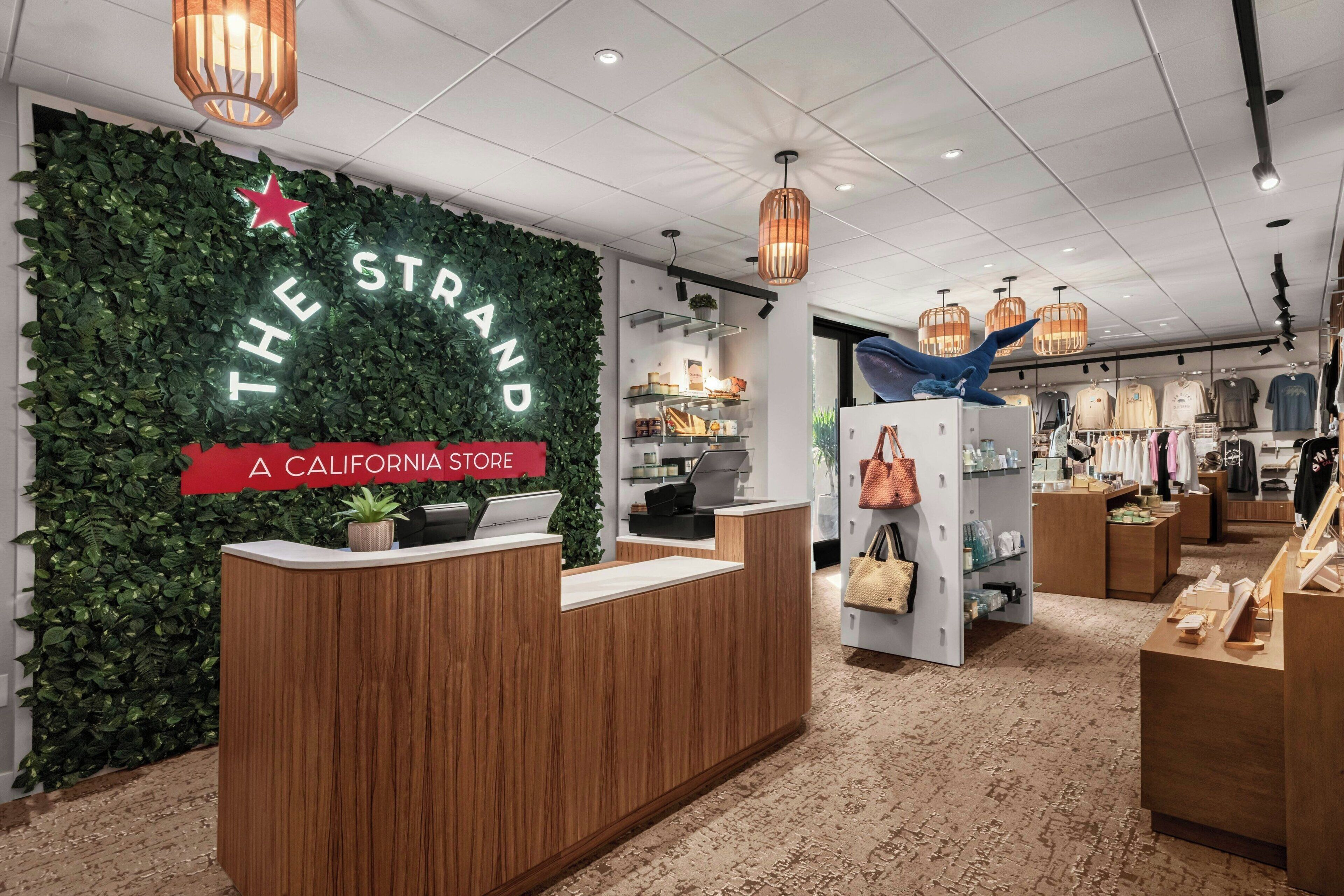 A store interior with a reception desk, a green wall with 'THE STRAND' signage, and various clothing displays.
