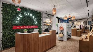 A store interior with a reception desk, a green wall with 'THE STRAND' signage, and various clothing displays.