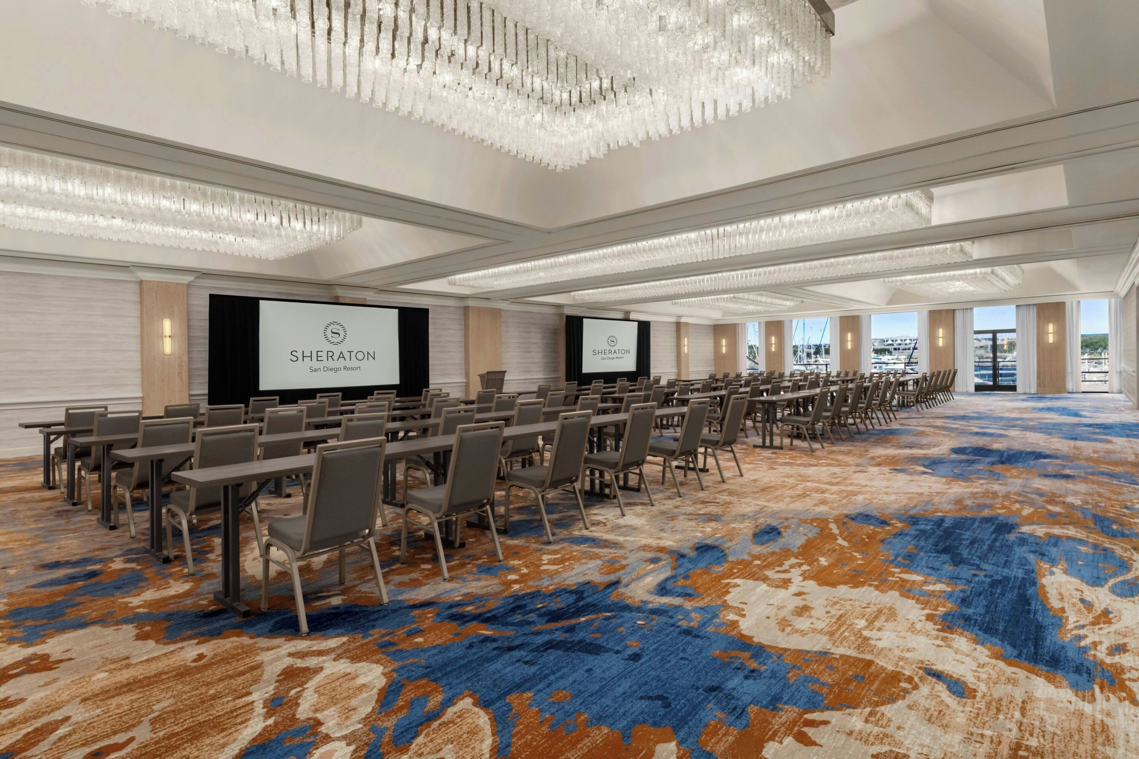 A Sheraton San Diego Resort conference room with a large screen, rows of tables and chairs, and a patterned carpet.