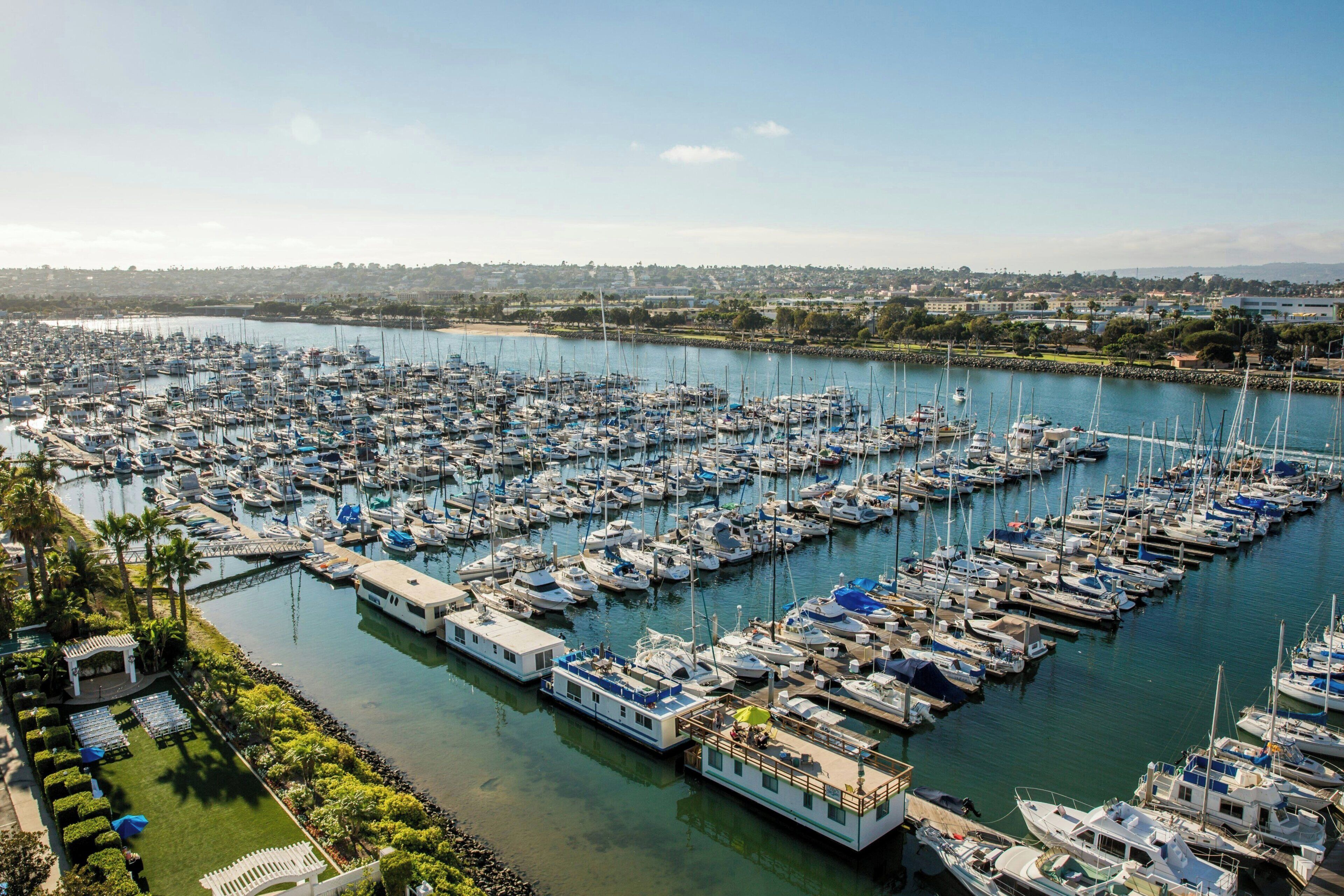 A marina with numerous boats docked in a structured layout, surrounded by greenery and a clear sky.