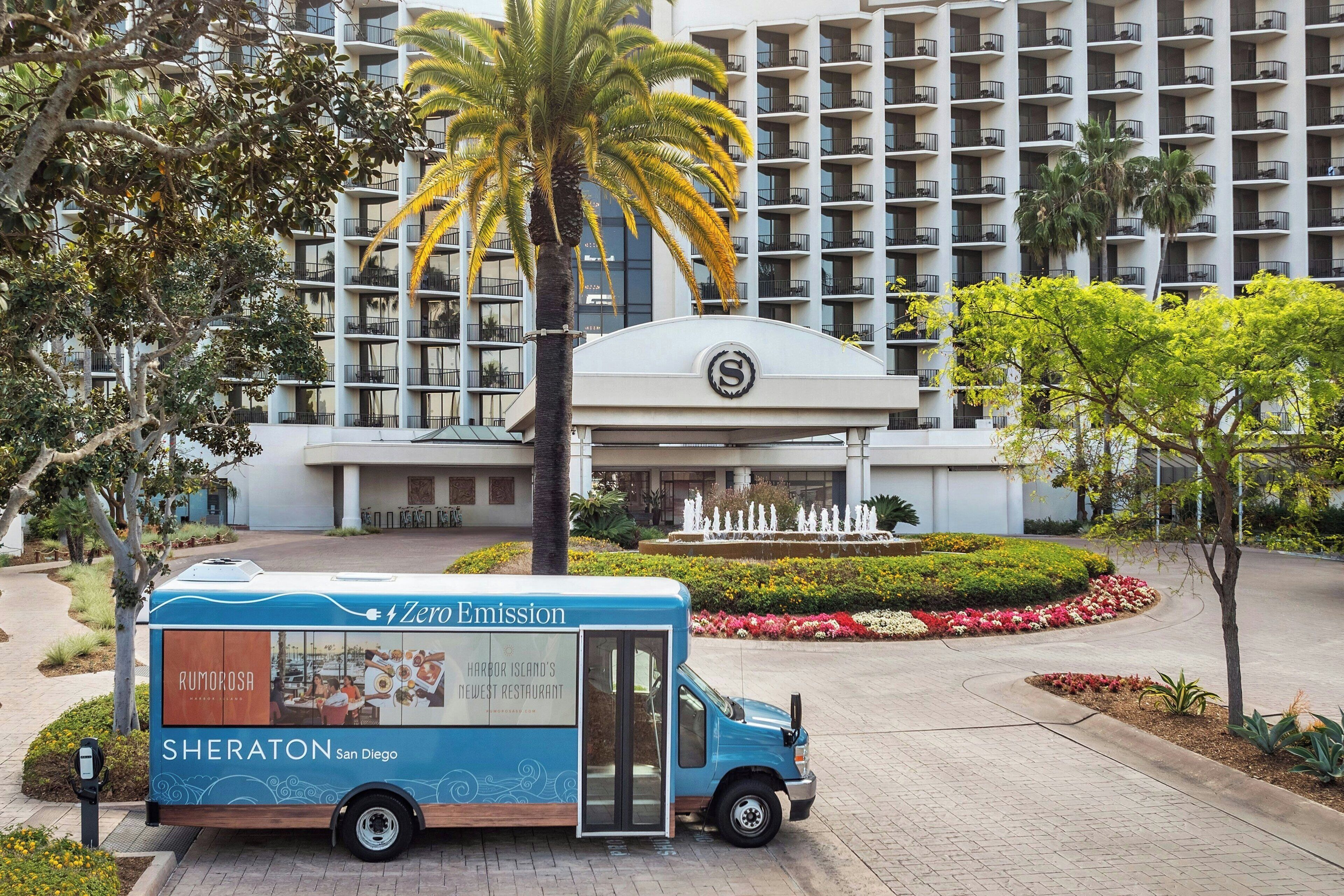 Un camión de comida estacionado frente a un hotel, con una palmera y una fuente al fondo.
