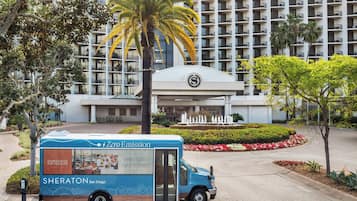 A food truck parked in front of a hotel with a palm tree and a fountain in the background.