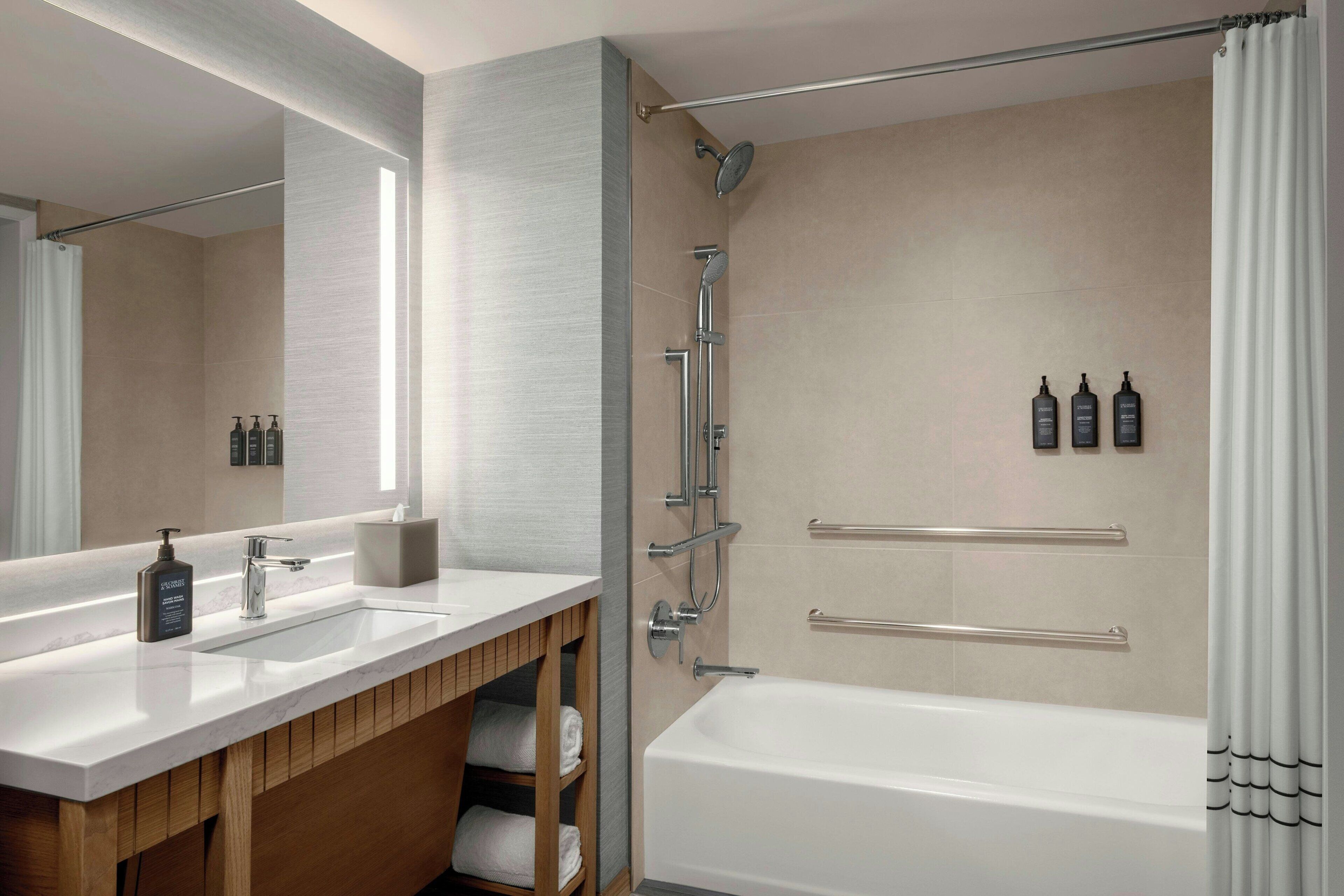 A modern bathroom with a large mirror, two sinks, a bathtub, and a shower.