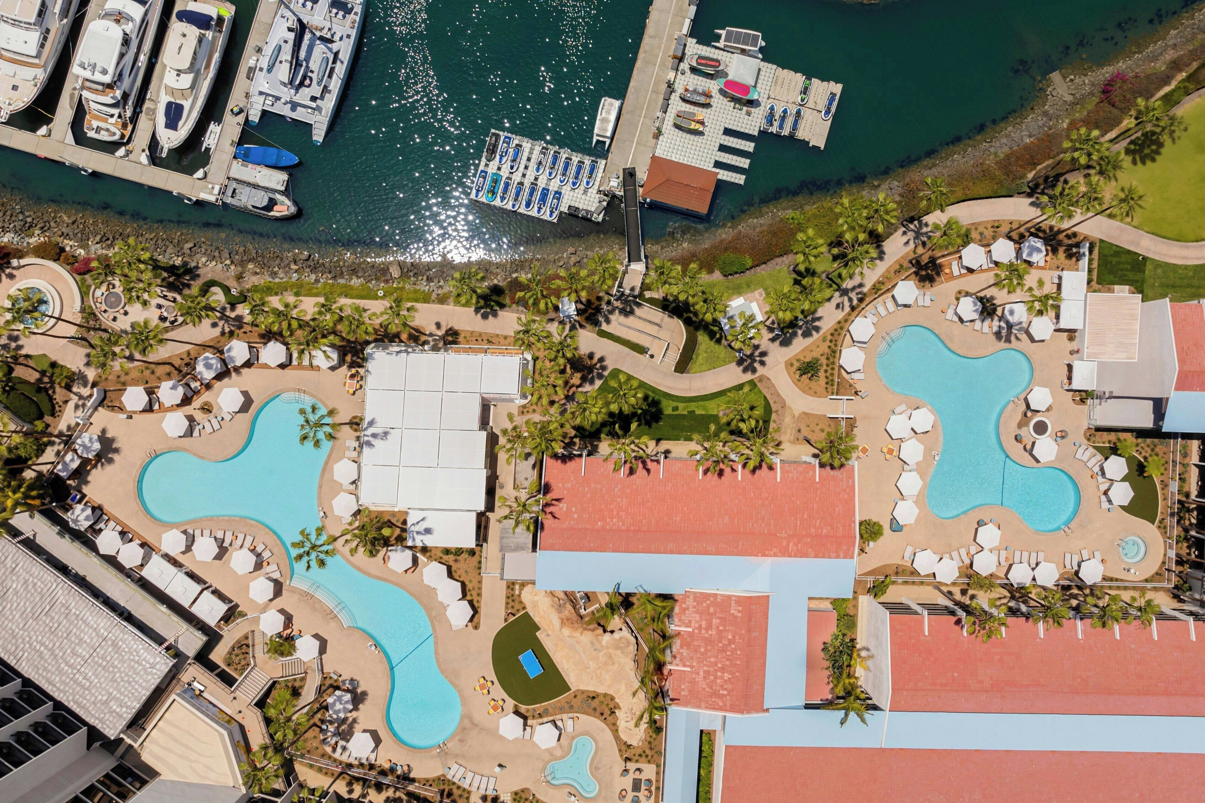 Vista aérea de un complejo turístico con varias piscinas, un puerto deportivo con barcos y diversas zonas de estar al aire libre.