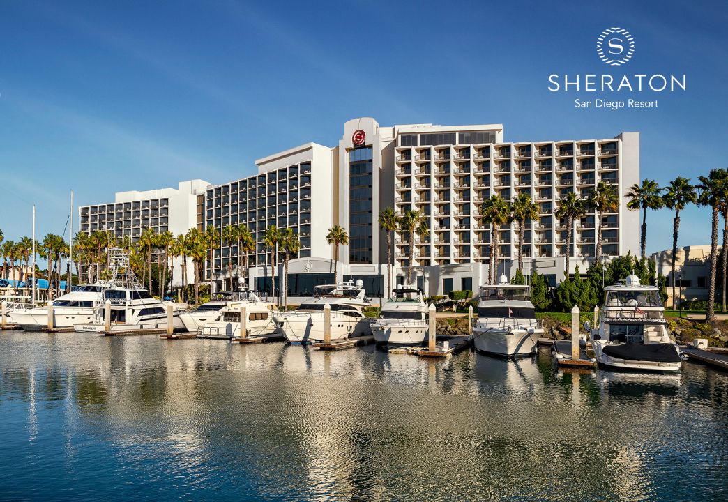 Un hotel de varios pisos, un puerto deportivo con barcos y palmeras.