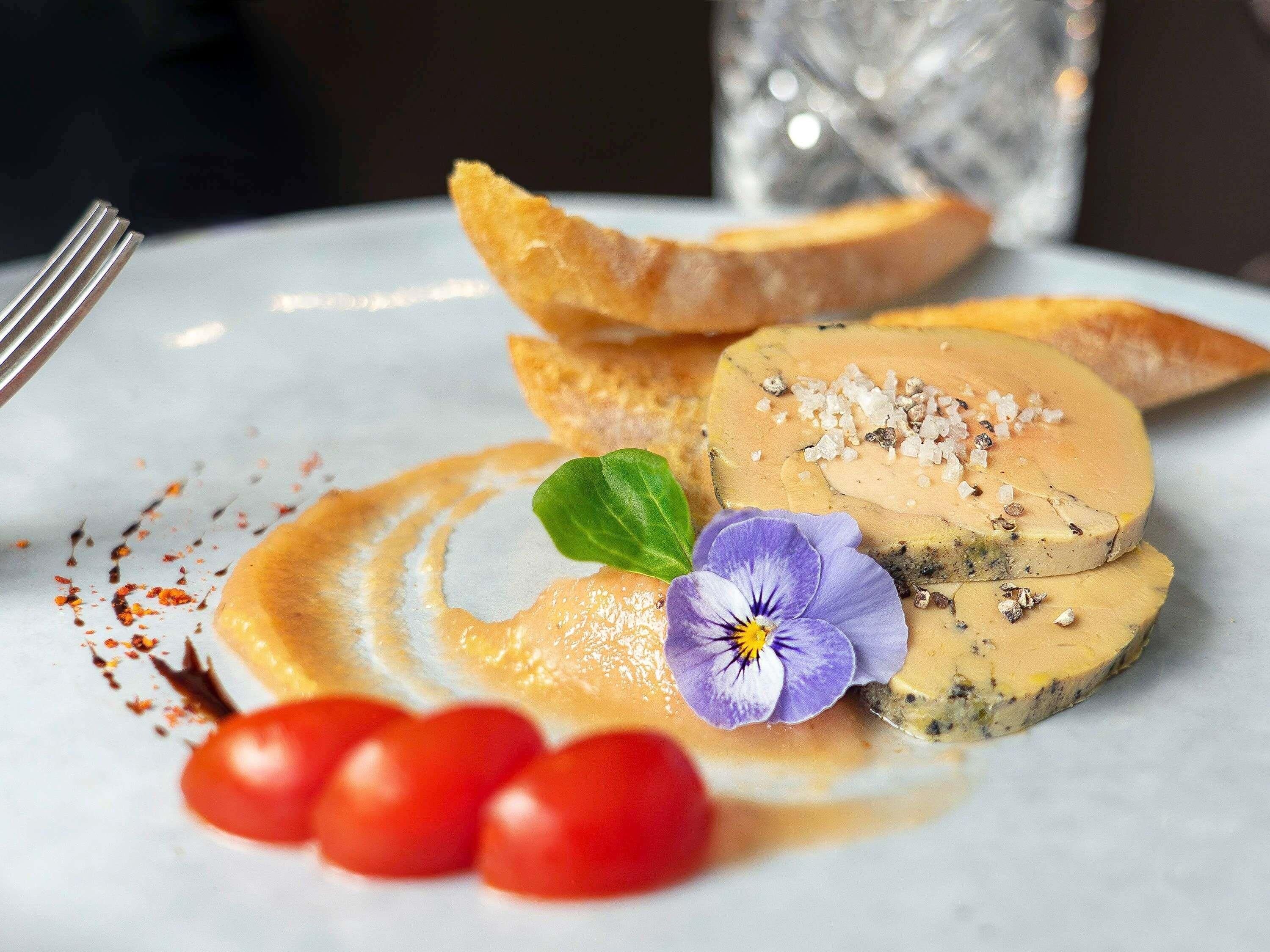 A plate with a food item, possibly a pâté, garnished with salt and a flower, accompanied by cherry tomatoes and a green leaf.