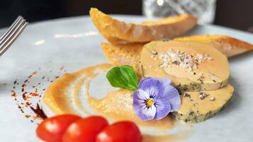 A plate with a food item, possibly a pâté, garnished with salt and a flower, accompanied by cherry tomatoes and a green leaf.