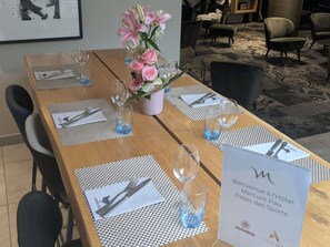 A hotel dining table set with placemats, cutlery, and glasses, with a sign indicating the hotel's name and location. - Mercure Pau Palais Sports (Pau)