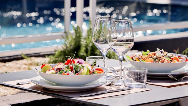 Spisebord med to salatportioner og to vinglas, med udsigt til en pool.