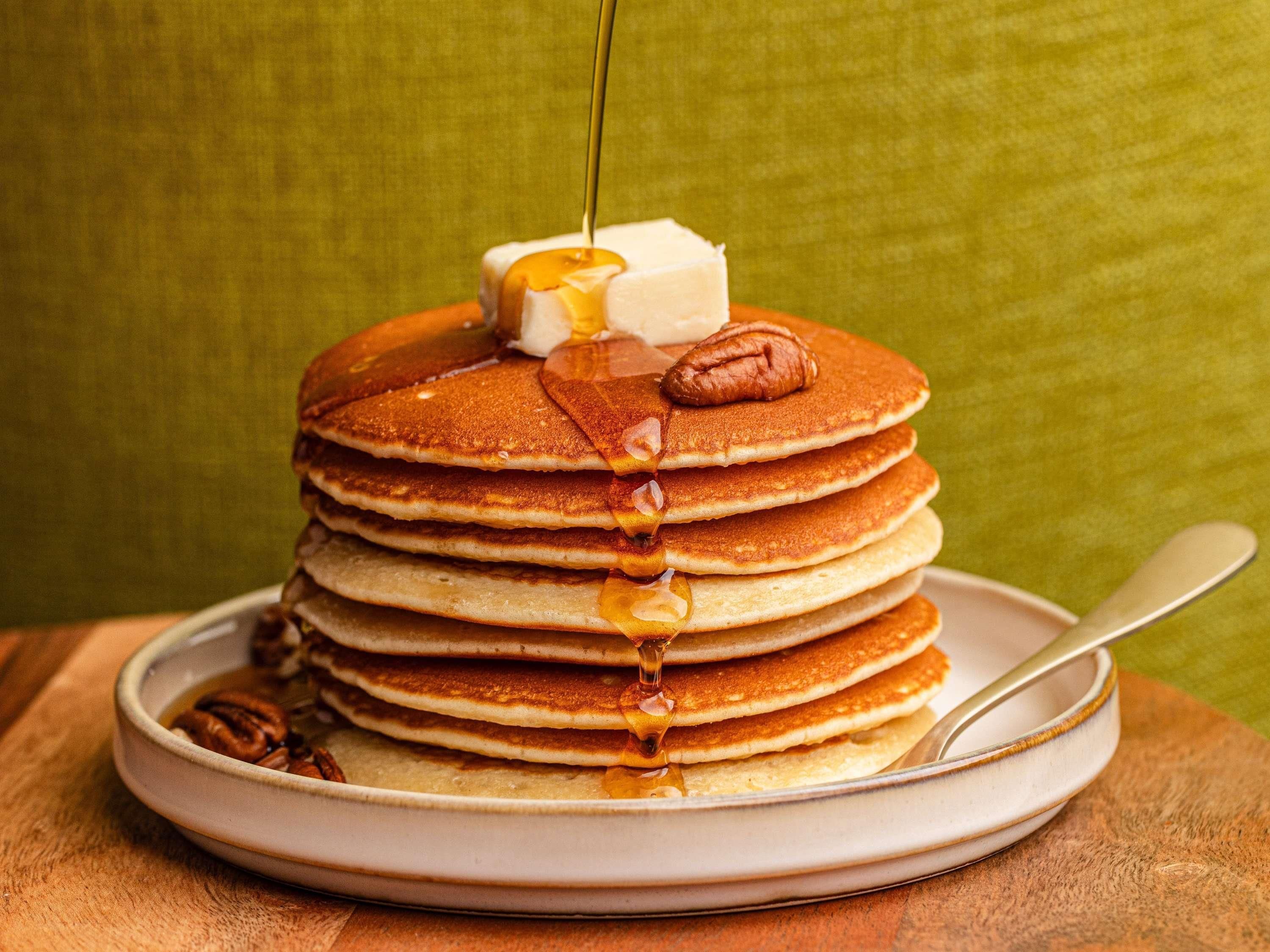 Een stapel pannenkoeken met siroop en pecannoten op een bord.