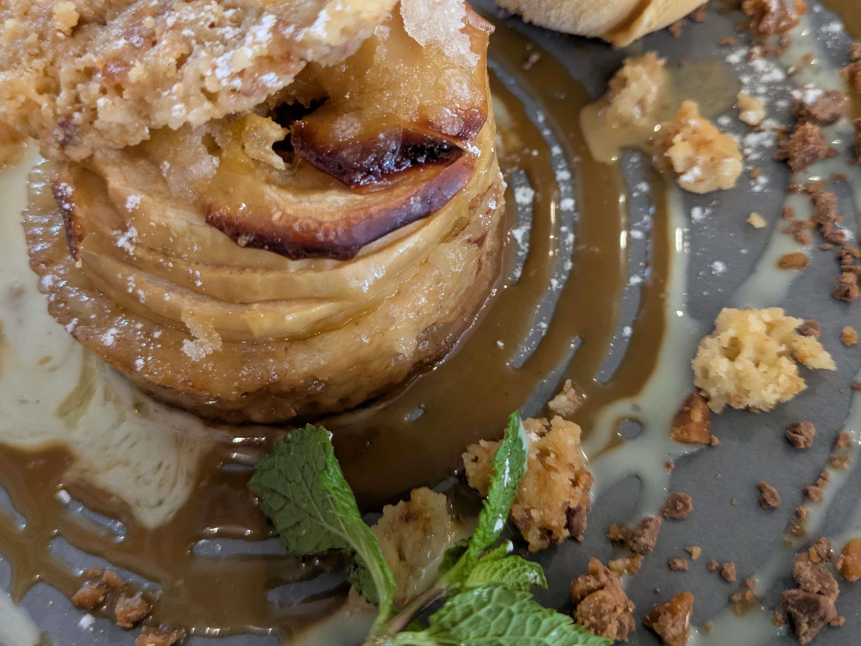 A dessert with caramel sauce and crumbled topping, garnished with mint leaves.