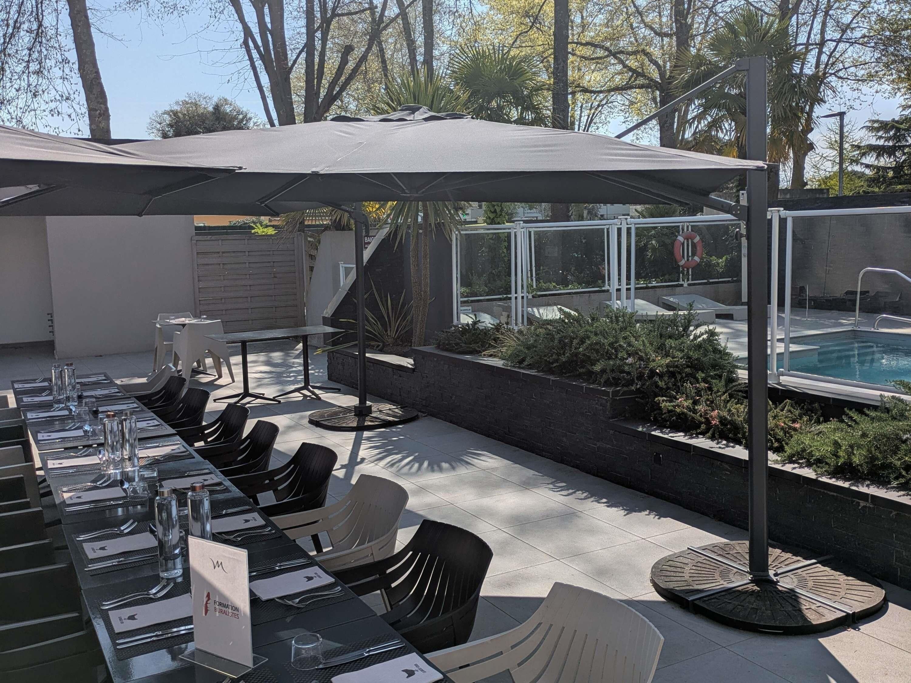 An outdoor dining area with tables and chairs, a pool, and a covered seating area.