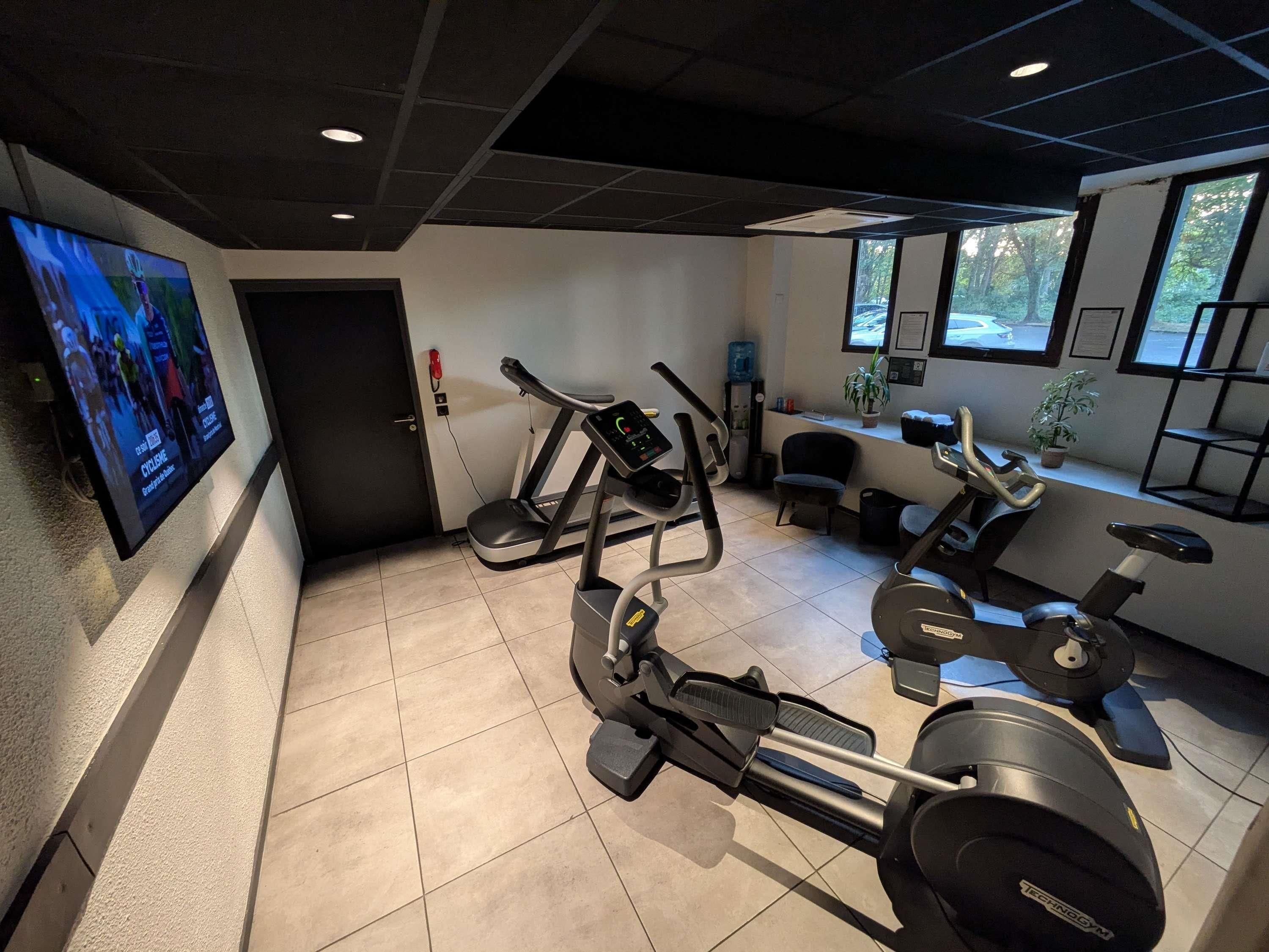 A gym with various exercise equipment, including treadmills and stationary bikes, and a television mounted on the wall.