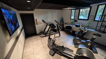 A gym with various exercise equipment, including treadmills and stationary bikes, and a television mounted on the wall.