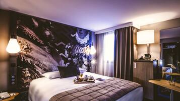 A hotel room with a large bed, a desk with a lamp, and a painting on the wall.