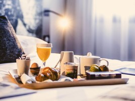 Bandeja de desayuno con croissants, un vaso de jugo de naranja, una taza y un recipiente pequeño de mermelada sobre una cama.