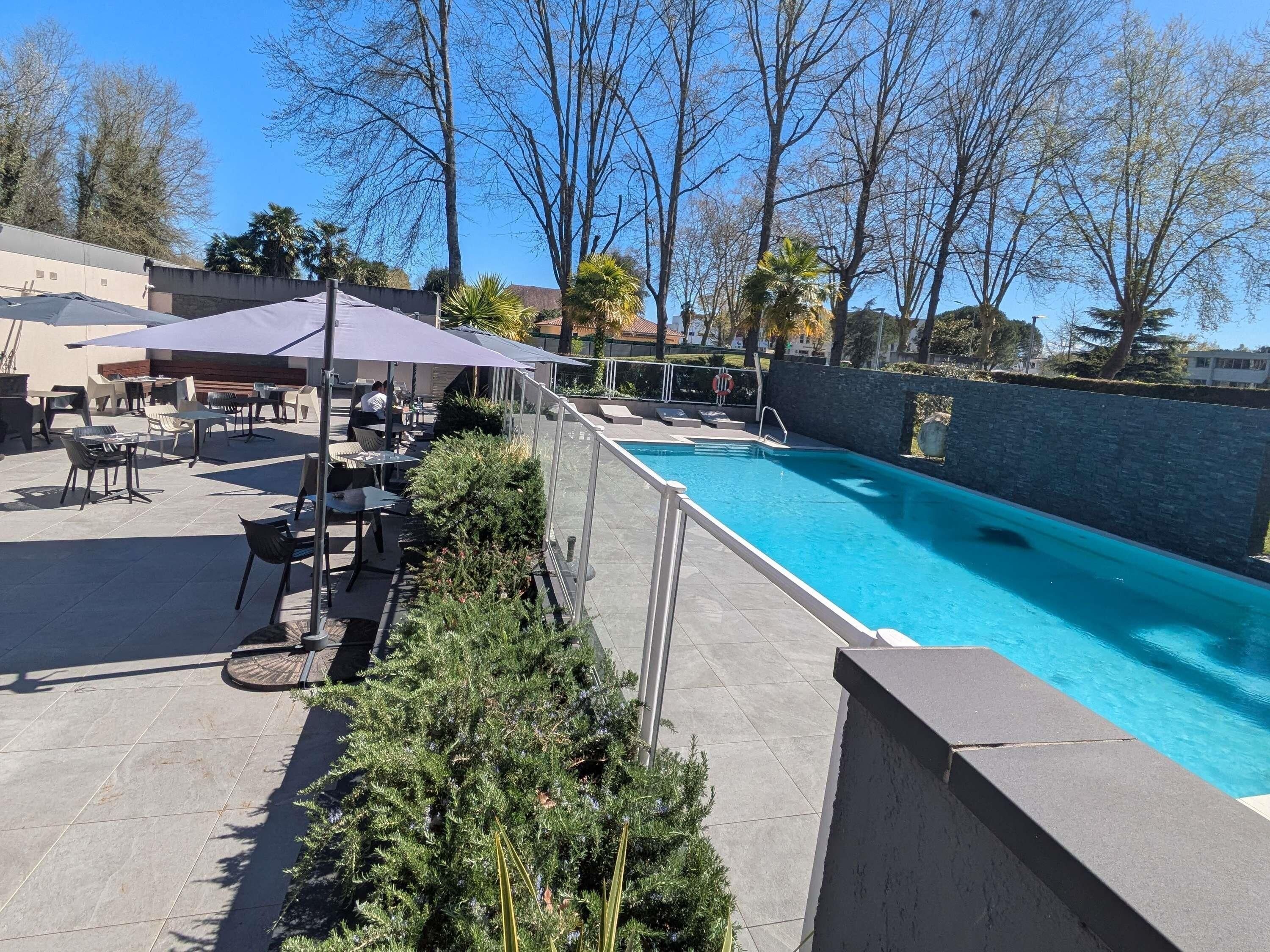 Piscina exterior con solárium de baldosas, rodeada por un muro de piedra bajo y una zona de patio con mesas y sillas.