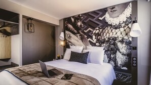 Et moderne hotelværelse med en stor seng, en bærbar computer på sengen og et dekorativt vægmaleri.