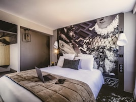 Una habitación de hotel moderna con una cama grande, un ordenador portátil sobre la cama y un mural decorativo en la pared.
