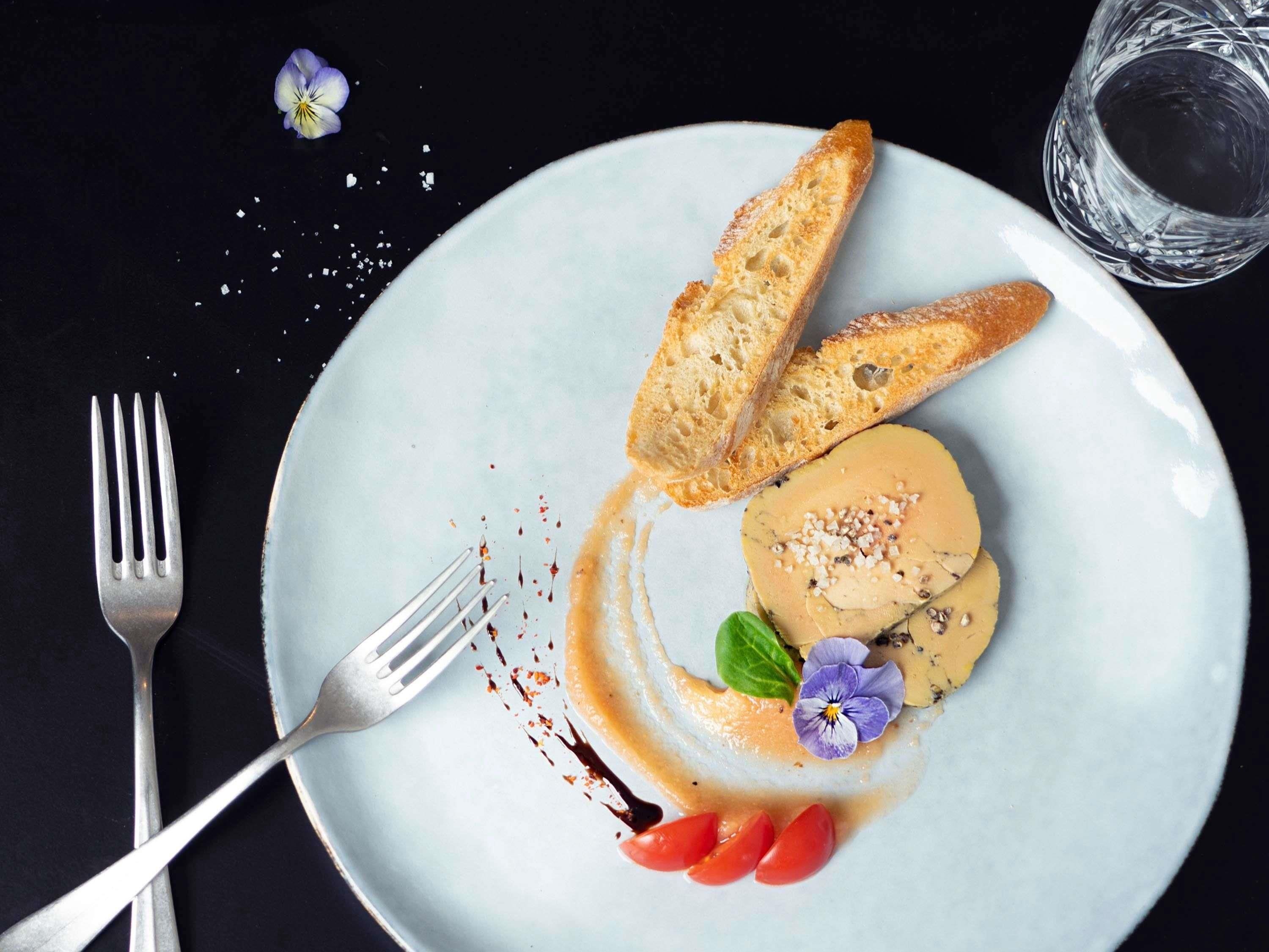 En tallerken med dessert, et glas vand og en gaffel på en mørk overflade.