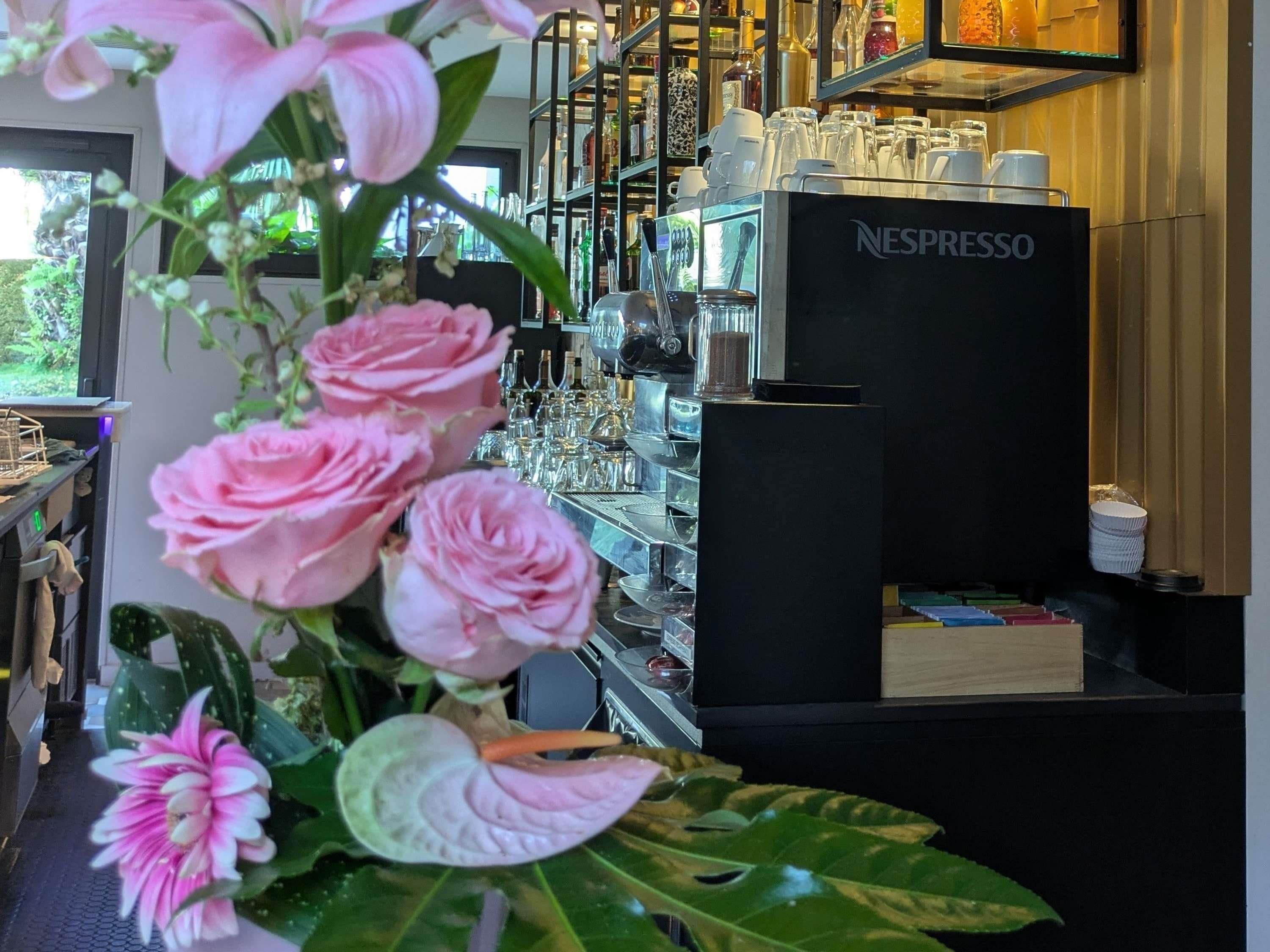 A bar area with a Nespresso machine, shelves with glasses and bottles, and a window with a view of greenery.