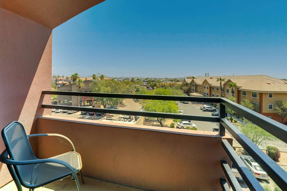 A balcony with a metal chair, a view of a parking lot, and buildings in the background.