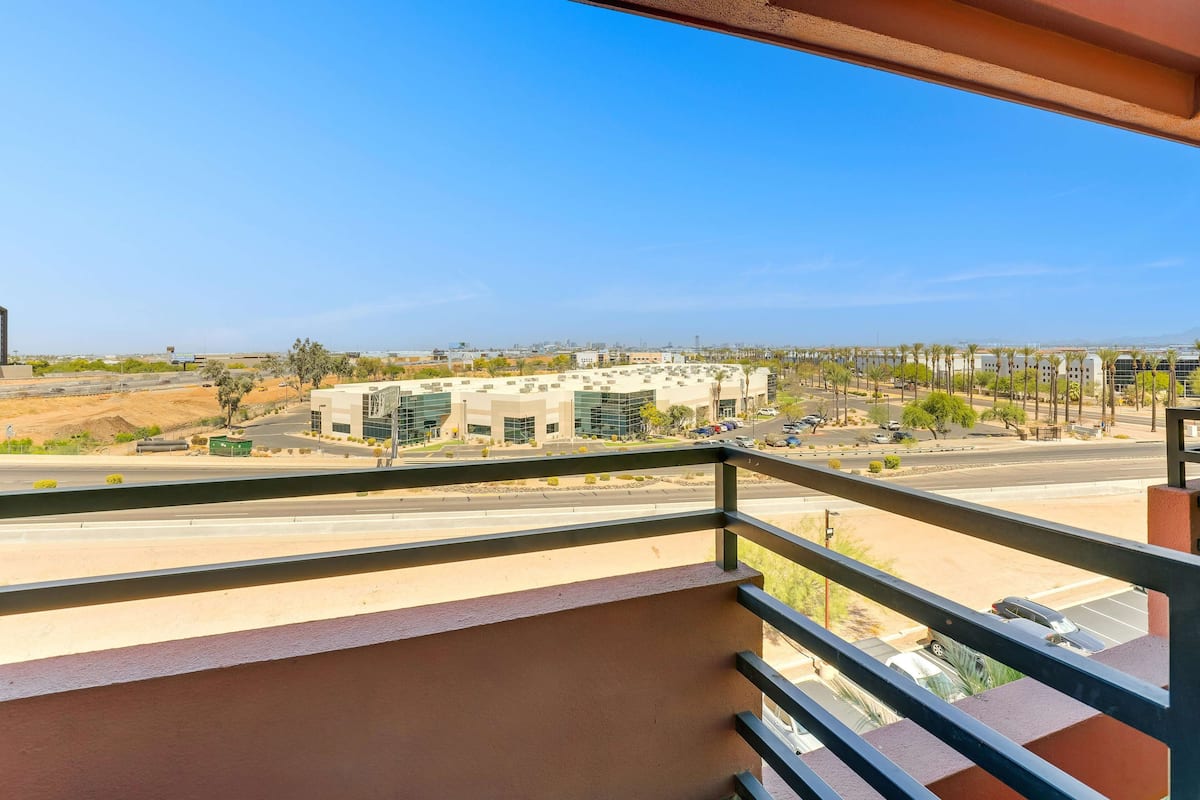 A balcony with a view of a modern building complex, a road, and sparse vegetation.