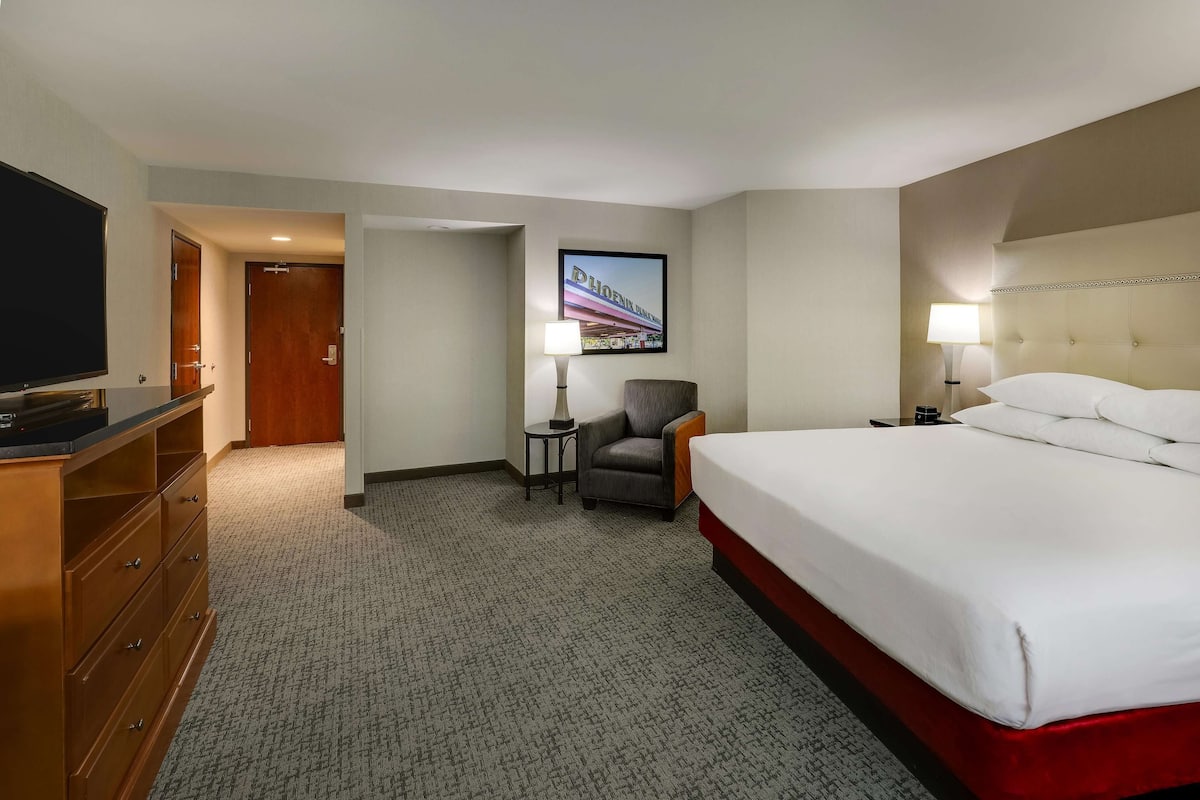 A hotel room with a bed, a TV, a chair, a lamp, and a framed picture on the wall.