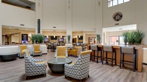 A spacious lobby with high ceilings, a reception area, and multiple seating arrangements including patterned chairs and a bar area. - Drury Inn & Suites Phoenix Airport (Phoenix)