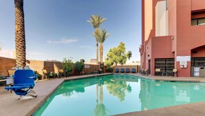 A swimming pool with lounge chairs and a barbecue grill, surrounded by palm trees and a building with a brick facade. - Drury Inn & Suites Phoenix Airport (Phoenix)