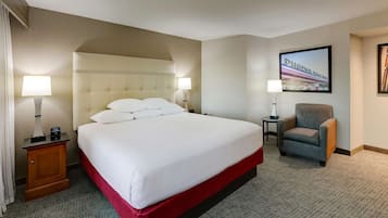 A hotel room with a large bed, two bedside tables with lamps, a chair, and a framed picture on the wall.